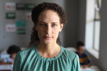 Fototapeta premium Close-up portrait of young female teacher with gray eyes standing in classroom