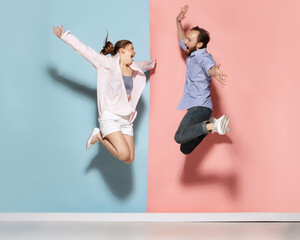 Astonished man and woman running, jumping isolated over blue and pink background. Human emotions,...