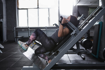 Female athlete doing lunges in hack squat gym machine, copy space