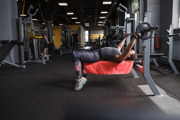 Full length shot of a sportswoman working out with barbell at gym, doing bench press
