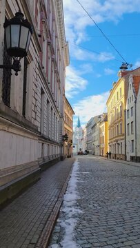 Vertical video. Walking walk through the streets of the old old town of Riga in the spring. Bright sun with long shadows on the paving stones. Medieval buildings and churches. Latvia