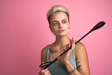 Tattooed blonde woman posing with black whip while enjoying of physical restrains during sex