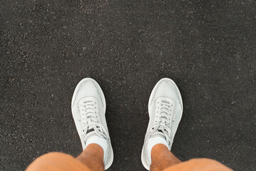 Close-up of man in shorts wearing sports stylish white summer sneakers standing on dark asphalt in...