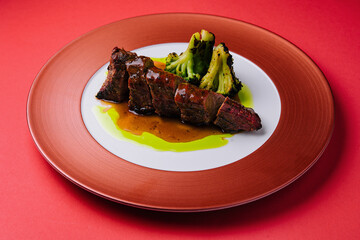 Roasted pork with sauce and broccoli on red plate