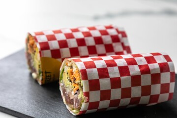 Closeup view of a sushi burrito wrapped in red and white checkered parchment paper
