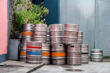 A stack of metal beer barrels. The containers standing by the road have orange, blue and red line markings. Irish landscape.