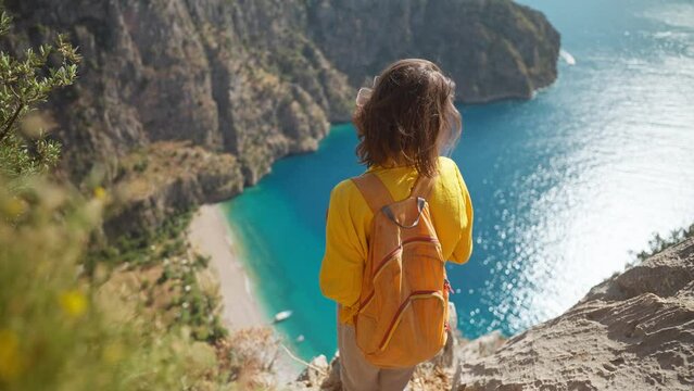 aerial top view woman traveler with blowing hair enjoying beautiful view of Butterfly Valley from edge of cliff on mountain top, Butterfly Valley in city of Oludeniz, Fethiye in western Turkey