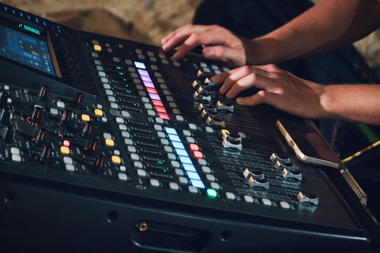 Shot of a multi-track sound mixer for live events with a man's hands on the console pushing fader buttons
