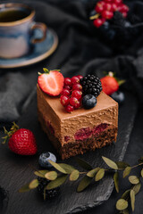 Delicious chocolate cake decorated with fresh berries on wooden black table