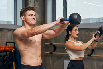 Naklejka premium Serious male and female holding hard kettlebell during physical exercise in fitness center