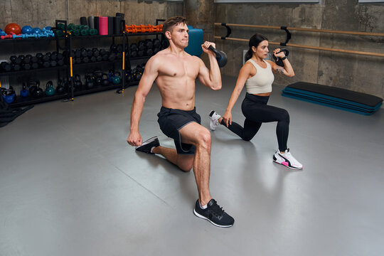 Male and female athletes lifting metal kettlebell with one hand from bent knee position