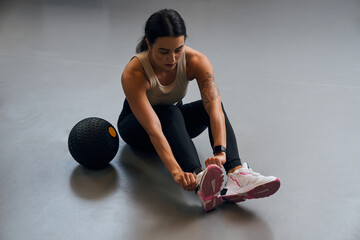 Focused female person correcting her shoes while preparing to the hard training