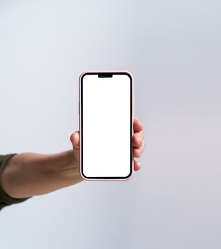 Hand of mature woman holding smartphone with white screen isolated on white background. Modern phone with touch screen in woman hand. Close up. Mock up mobile app advertising. No face visible.