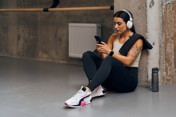 Naklejka premium Young sporty well trained woman listening to music on smartphone in gym