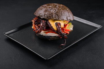 Appetizing marinated octopus burger on a black tray