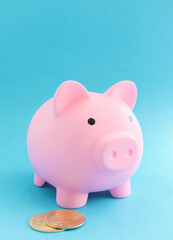 Pink piggy bank and coins on blue paper background saving money and financial ideas