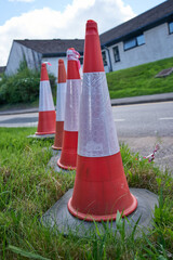 four red and white reflective traffic cones lined up on a grass verge in a residential area
