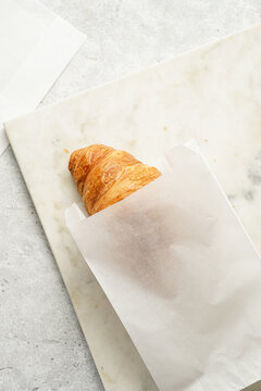 Two french soft croissants in white breakfast paper bags for take-away on marble board on grey surface