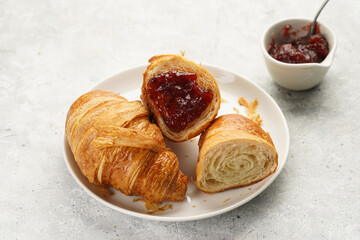 Two french soft croissants with jam on a white plate on a marble tray, a cup of black coffee in white sophisticated cup, milk, sugar