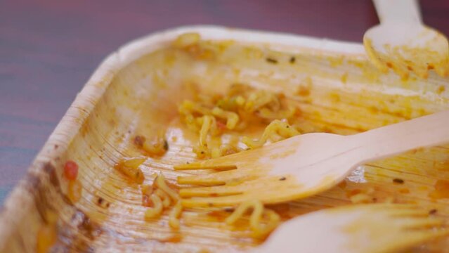 Closeup shot of empty disposable plate with leftover noodles and fork. A dirty empty plate of pasta or spaghetti and a fork on a table. Used cutlery after eating symbolize the end of lunch or dinner.