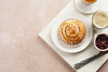 A round cinnamon pastry on a white plate on marble board on light pink background, cup of coffee, jam, milk