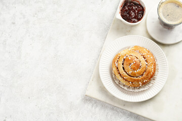 A round cinnamon pastry on a white plate on marble board on light pink grey, cup of coffee, jam, milk, copy space for text