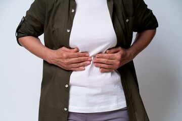 close up. Mature woman having stomach problems experiencing pain in dark green shirt isolated on white background. No face visible middle aged woman with abdominal pain. Healthcare concept. - obrazy, fototapety, plakaty