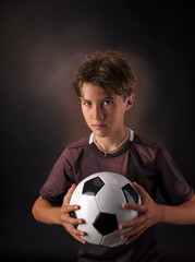 Child posing in the foreground on a black background, with a classic white soccer ball with black pentagon shaped inserts.