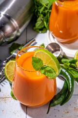 Carrot Ginger Margarita cocktail with lime, mint and hot chili pepper, original vegetable spicy drink on white tiled background copy space
