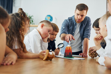 Fototapeta premium Looking at the model of volcano. Group of children students in class at school with teacher