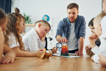 Fototapeta premium Looking at the model of volcano. Group of children students in class at school with teacher