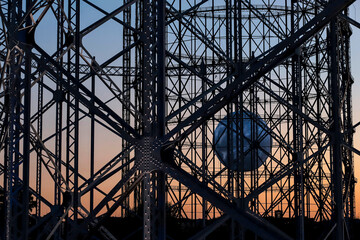 Metal structure of the disused gasometer in Rome, in the center there is a large white ball that resembles the moon, in the background sky at sunset.