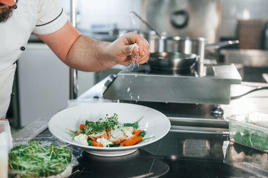 Giving salt to the salad. Professional chef preparing food in the kitchen