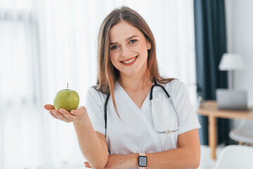 Woman holding an apple. Professional medical worker in white coat is in the office