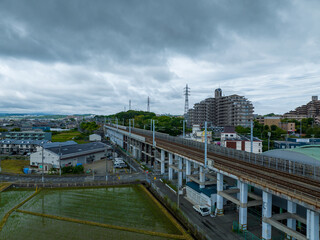 Elevated train tracks next to rice fields under dark grey storm clouds