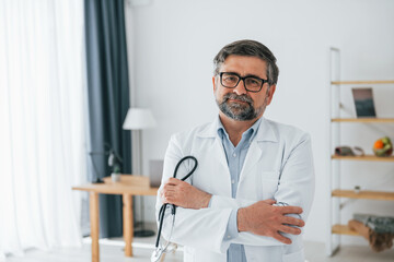 Male doctor is with stethoscope. Professional medical worker in white coat is in the office