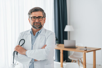 Standing and holding stethoscope. Professional medical worker in white coat is in the office