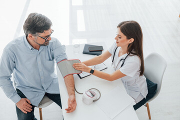 Measuring blood pressure and checking the document. Professional medical worker in white coat is in the office