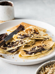 Pancakes with chocolate cream and nuts on a white plate. Thin pancakes, pancakes. Delicious breakfast or snack. The background of the food recipe. Vertical orientation.