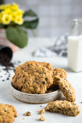 Homemade oatmeal cookies with chocolate chips in a small plate on a rustic table. On the background of a flower, bottles of milk, scattered chocolate and cookie crumbs.