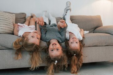 Girls laying down on the sofa upside down and smiling. Group of children is together at home at daytime