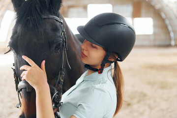 Close up view. A young woman in jockey clothes is preparing for a ride with a horse on a stable