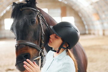 Obraz premium Embracing the animal. A young woman in jockey clothes is preparing for a ride with a horse on a stable