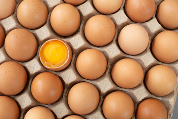 Flat lay Close-up view of raw chicken eggs in egg paper box. One egg cracked showing the yolk. Top view Natural organic egg. Fresh chicken eggs, organic eggs, eggs for food ingredients, and healthy fo