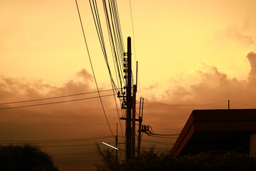 Silhouette electrical cable and pole in living village against orange sky, tangled mess of...