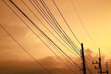 Silhouette electrical cable and pole in living village against orange sky