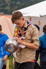 Boy scout cleaning kitchenware in a campsite - obrazy, fototapety, plakaty