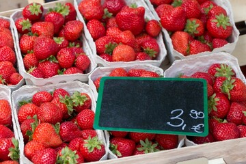 Strawberry market baskets with many delicious red strawberries. Cups of fresh sweet quality strawberries at marketplace. Local bio fruit sale with euro price tag and blank black label copyspace