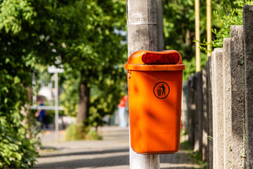 Fototapeta na wymiar Orange trash bin in an urban area on a sidewalk full of green trees
