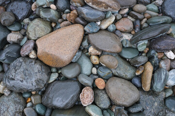 Background of rounded river stones of different sizes in the water. River bank